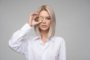 Junge Frau hält sich Bitcoin vor ein Auge